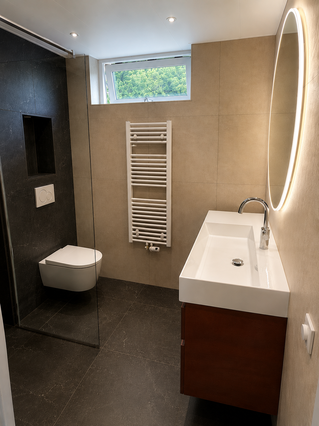 Complete badkamer in Hoogeveen met donkere vloer, warm wastafelmeubel en ovale spiegel