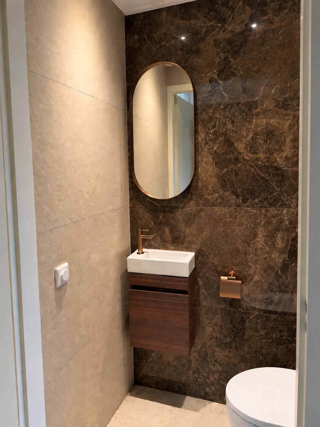 Toiletruimte met compact donker fonteinkastje, bronzen kraan en ovale spiegel