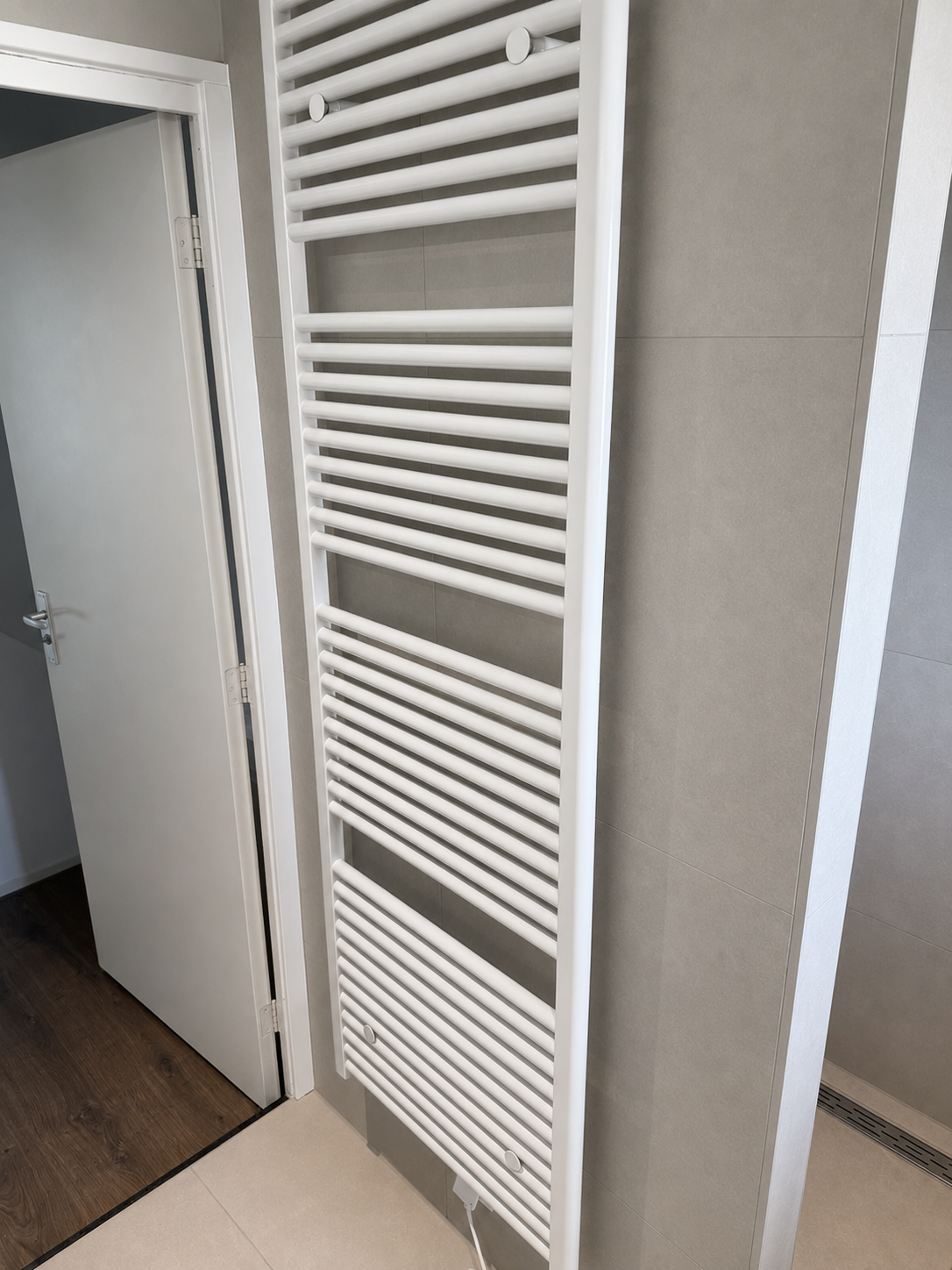 Witte designradiator op een betegelde badkamerwand